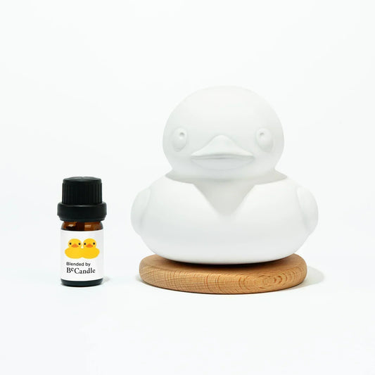 White ceramic duck aroma stone on wooden base with small essential oil bottle labeled BeCandle